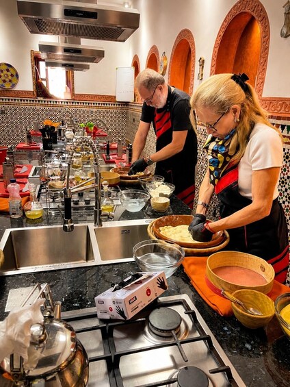 A kitchen with two people preparing food, a stove, and various cooking utensils. 2