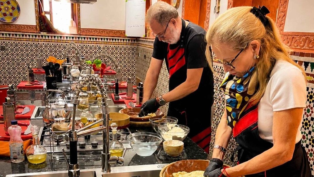 Two people preparing food in a kitchen with a tiled backsplash and various cooking utensils. 2