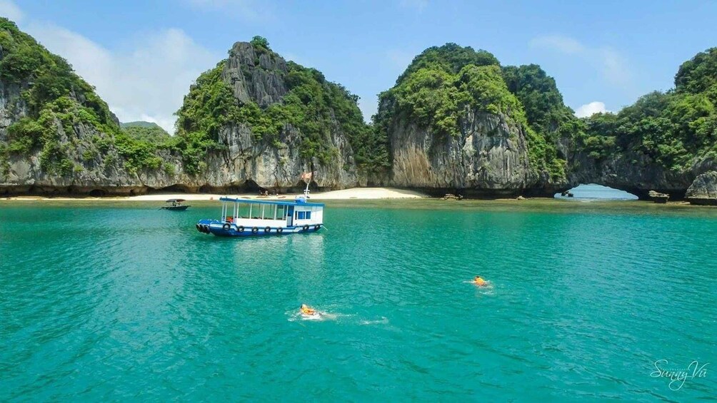 A boat on turquoise water with a swimmer in the distance and a beach with limestone cliffs in the background. 1