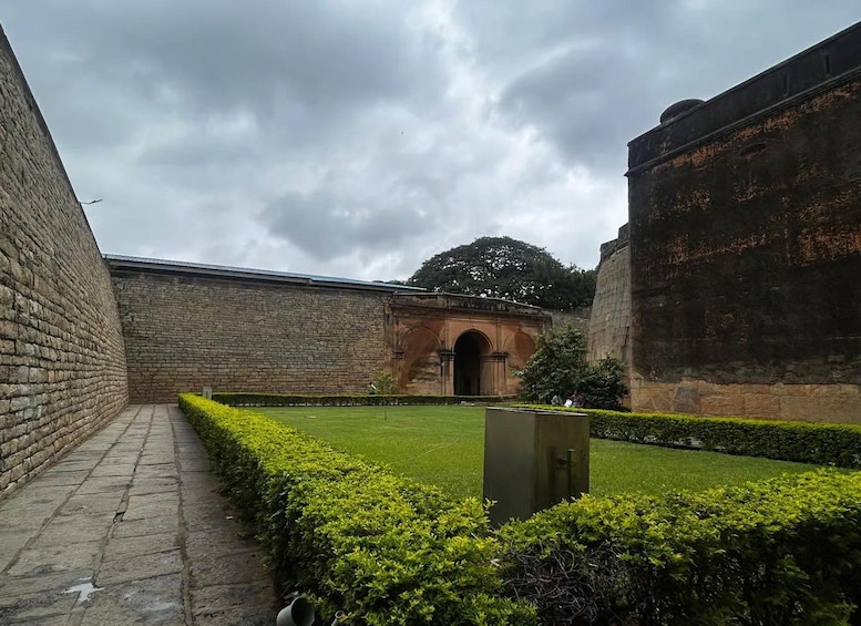 A stone courtyard with a central archway, surrounded by neatly trimmed hedges and a brick wall. 2