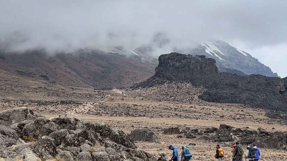 A group of hikers on a rocky trail with a mountain in the background. 2