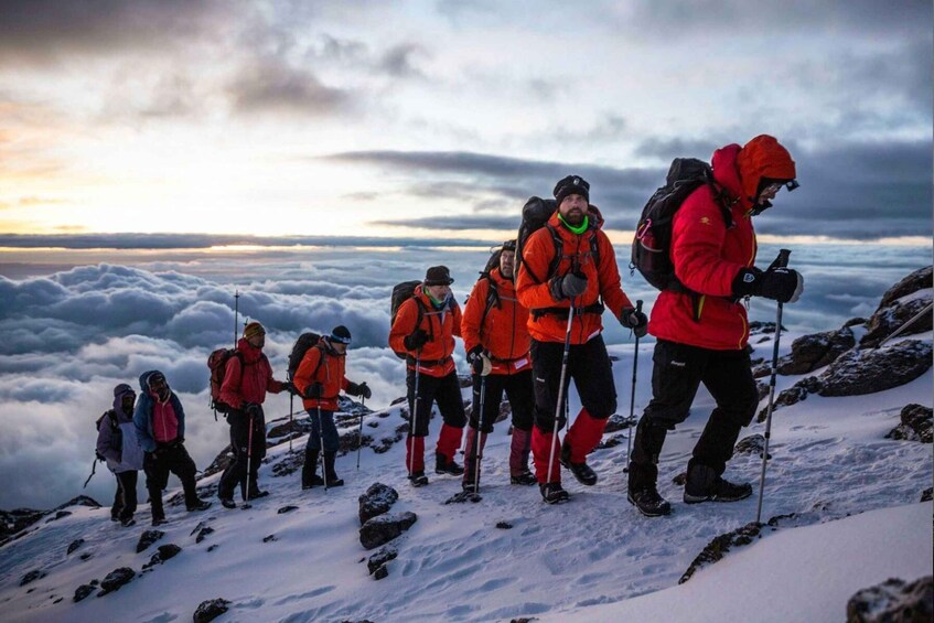 A group of hikers on a snowy mountain trail with a cloudy sky. 3