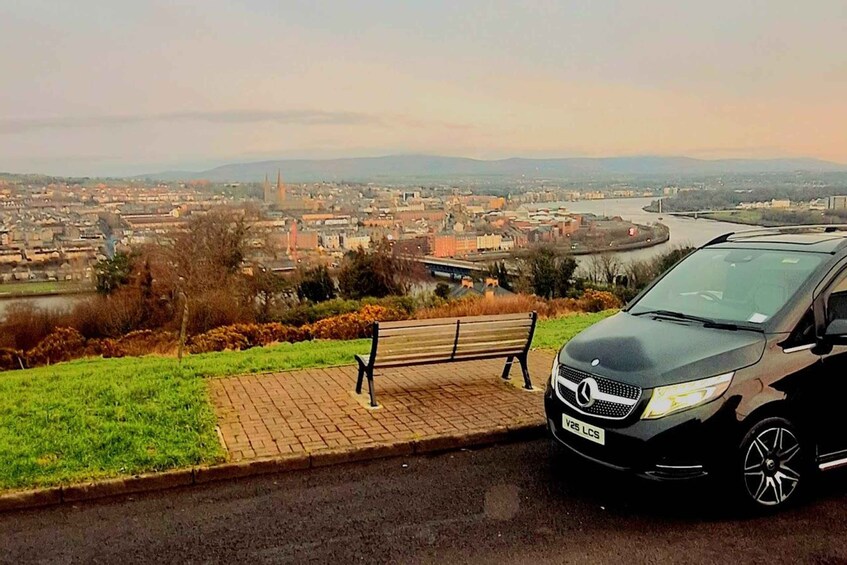 A black car parked on a roadside with a bench and a river in the background. 1