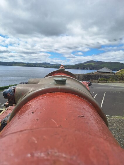 A red pipe with a valve, a road, a body of water, and distant hills. 5