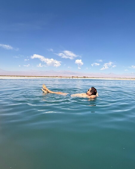 Two people floating in calm, turquoise waters with a clear sky and distant mountains. 1