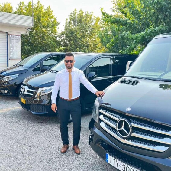 A man standing next to a black Mercedes-Benz SUV in a parking lot with other vehicles. 1