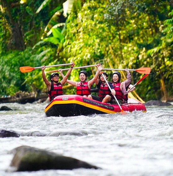 A group of people in a red inflatable raft on a river, wearing life jackets and paddles. 3