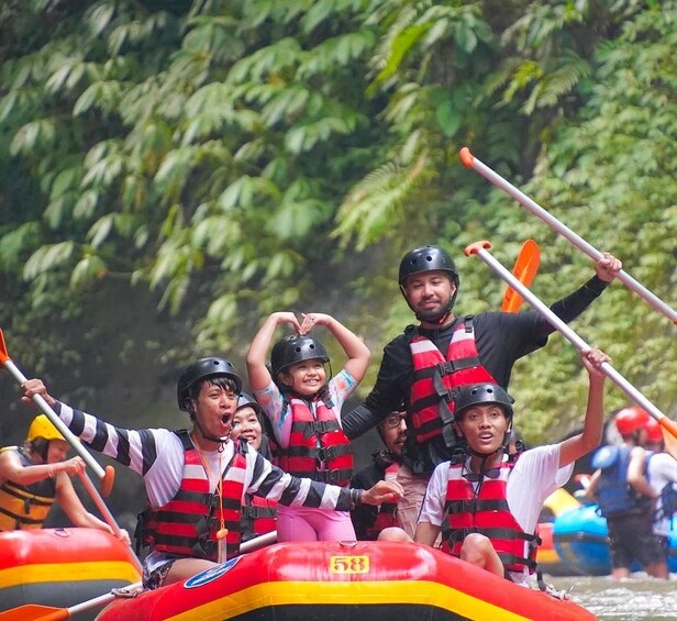 People in a raft with paddles, wearing life jackets and helmets, on a river surrounded by greenery. 5