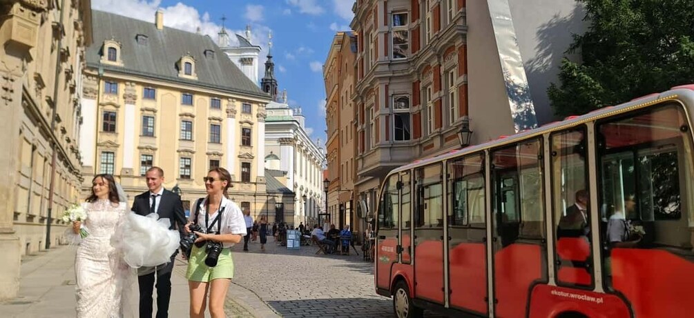 A wedding procession on a cobblestone street with historic buildings and a red bus. 5