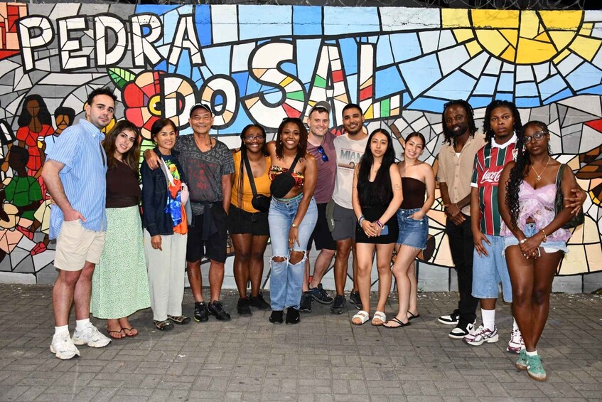 A group of people posing in front of a colorful mural with the text 'PEDRA DO SAL.' 1