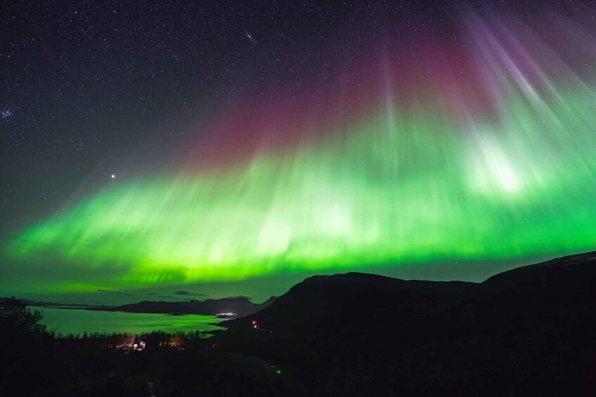 The Northern Lights over a mountainous landscape with a small settlement in the distance. 1