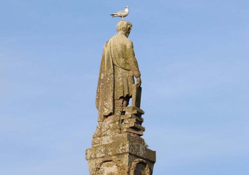A weathered statue with a bird perched on its head, set against a clear sky. 2
