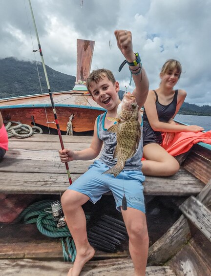 En person holder en fisk på en båd med et bjergrigt landskab i baggrunden. 1