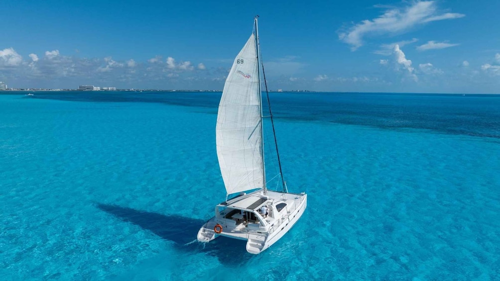 A sailboat on clear turquoise water with a distant shoreline and buildings. 1