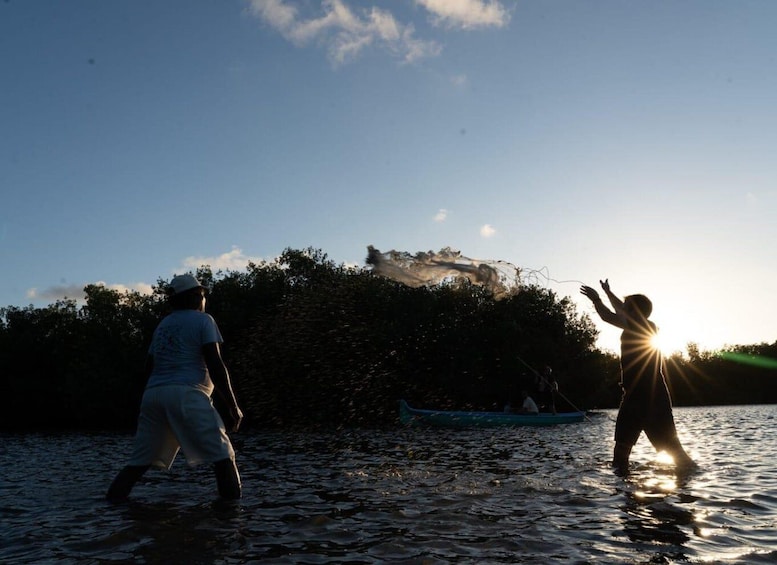 Two people walking in shallow water with a boat in the background and a hill with trees. 4
