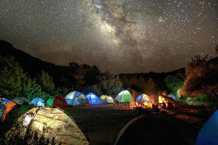 A night scene with multiple colorful tents under a starry sky, illuminated by a campfire. 5