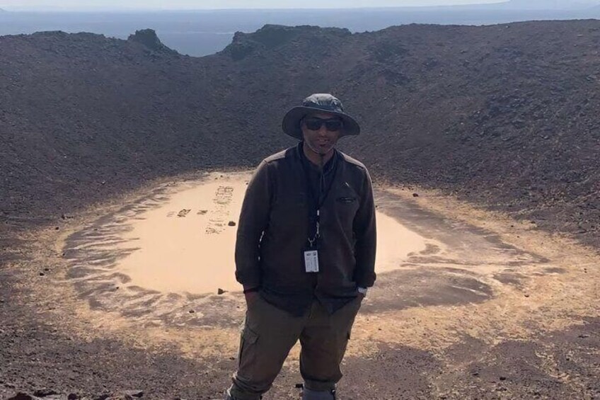 A person standing in a barren landscape with a circular pattern of footprints in the sand. 4
