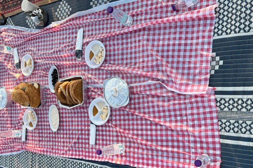 A picnic setup with a checkered blanket, food items, and a patterned rug. 5
