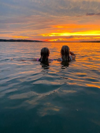Two people swimming in a body of water during sunset. 1