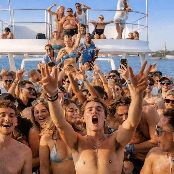 A group of people on a boat, some raising their hands, and a cityscape in the background. 1