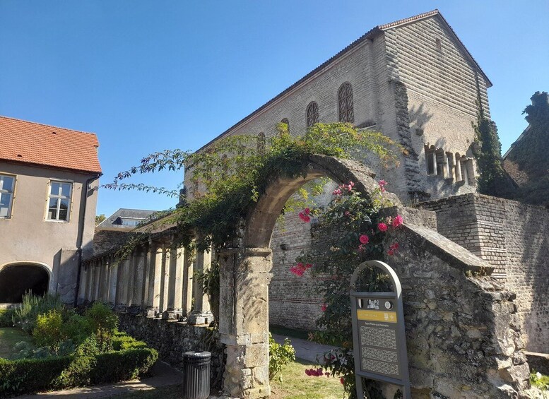 An old stone building with a red-tiled roof, an arched doorway, and a signboard. 1