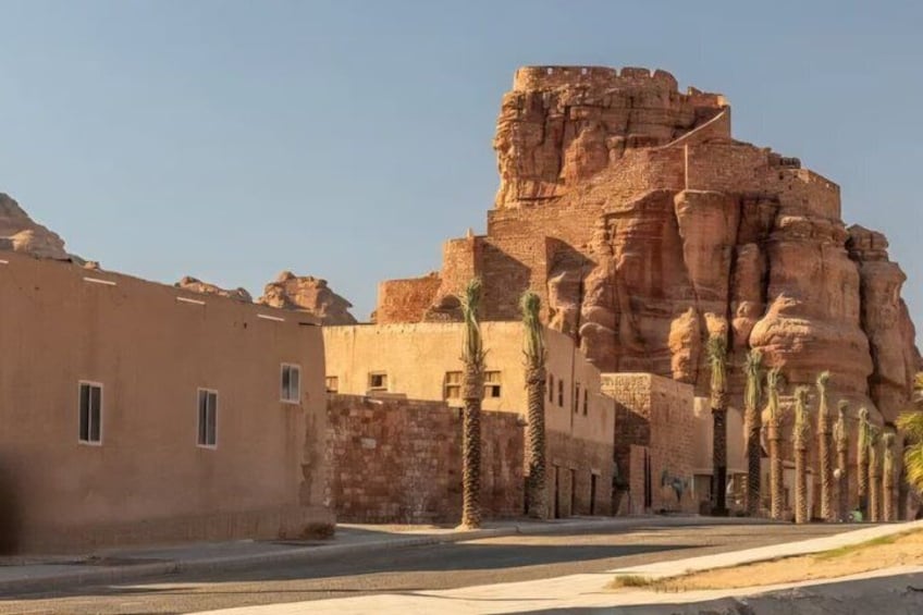 A desert landscape with a large rock formation, palm trees, and traditional buildings. 4