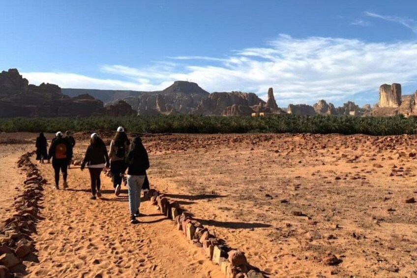 A group of hikers walking on a sandy trail in a desert landscape with rock formations in the background. 3