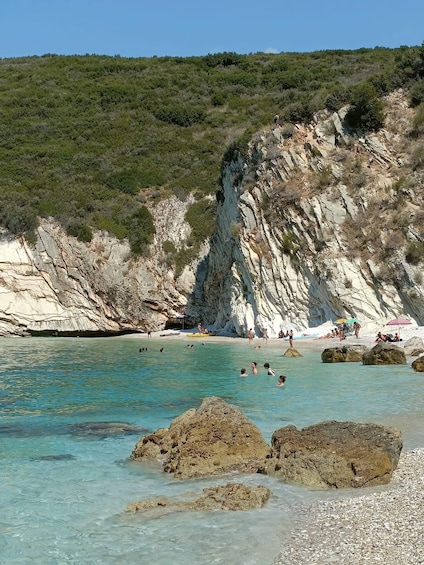 A coastal beach with clear turquoise water, rocky outcrops, and people swimming and sunbathing. 4