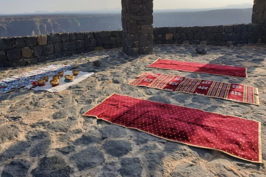 A stone structure with red carpets and bowls on the ground. 2