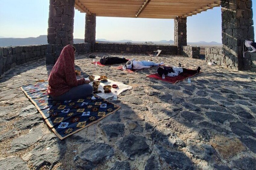 A person sitting on a blanket under a stone structure with a view of the landscape. 3