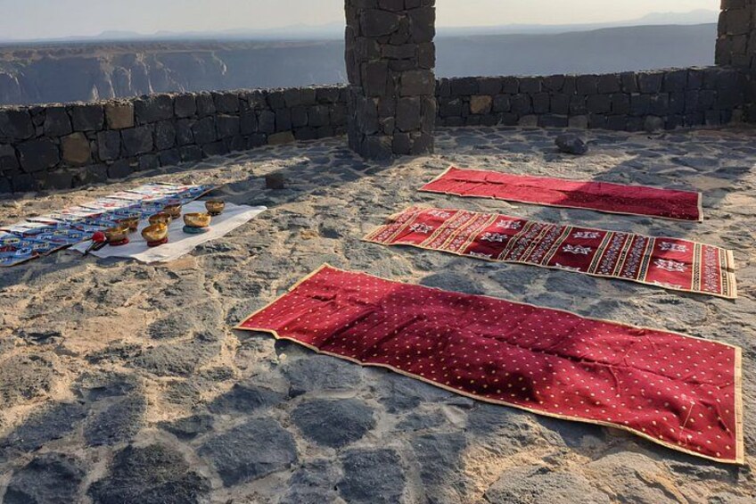 A stone structure with red carpets and bowls on the ground. 2