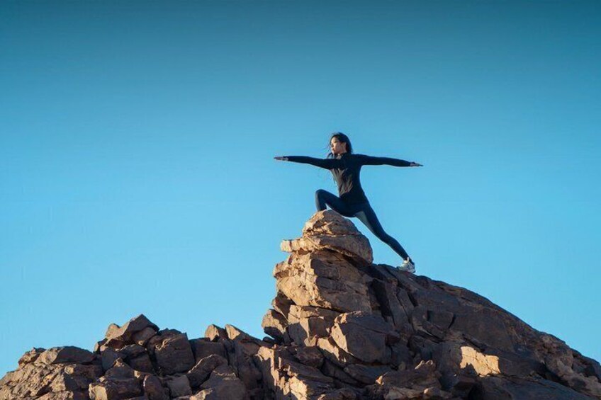 A person in a black outfit standing on a rocky outcrop with arms outstretched. 1