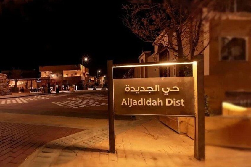 A nighttime street scene with a sign reading 'Aljazeera Dist' in Arabic. 3