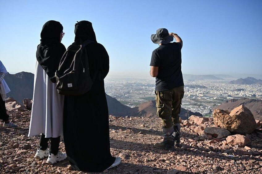 A group of people on a rocky mountain top overlooking a cityscape. 1