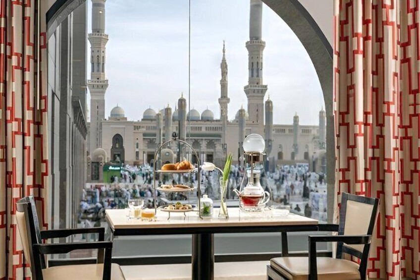 A table with food and drink, a view of a mosque with minarets, and patterned curtains. 2