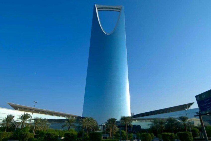 A tall, modern skyscraper with a curved top, surrounded by palm trees and other greenery. 3