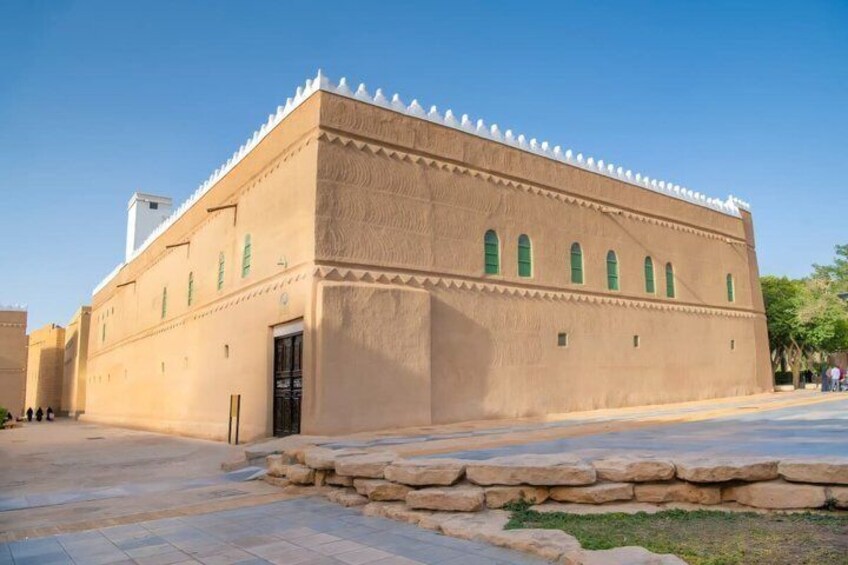 A large, beige building with green windows and a white-topped roof, surrounded by a paved area and stone walls. 4