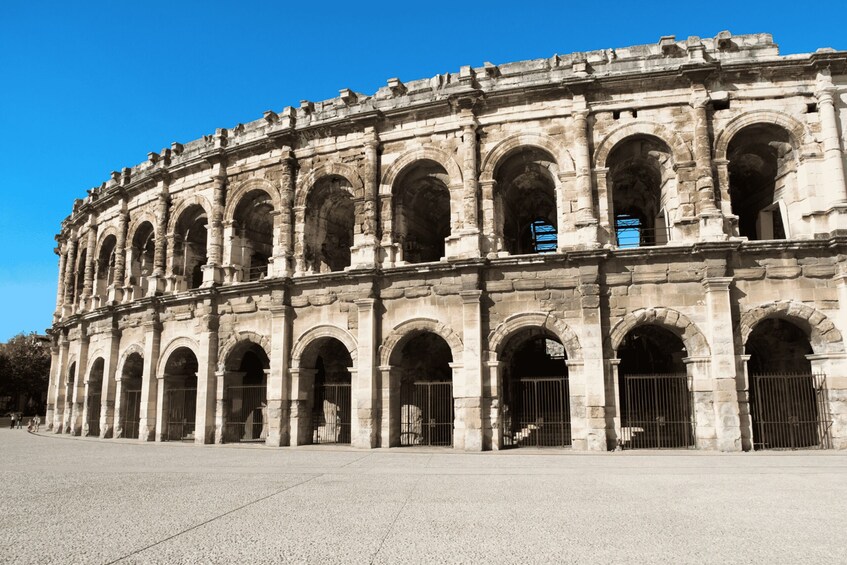 A historic stone building with multiple arches and columns, featuring a clear blue sky in the background. 2