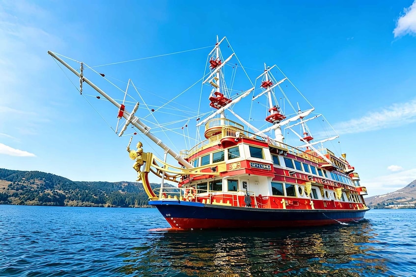 Un barco grande y colorido con múltiples cubiertas y mástiles, navegando sobre un lago tranquilo con colinas al fondo. 1