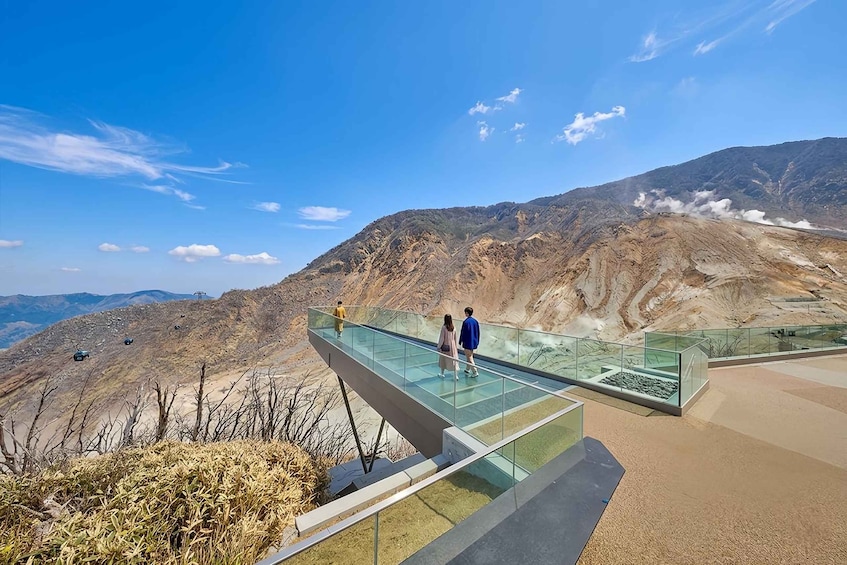 Un puente de cristal con gente caminando, con vistas a un paisaje montañoso bajo un cielo despejado. 4