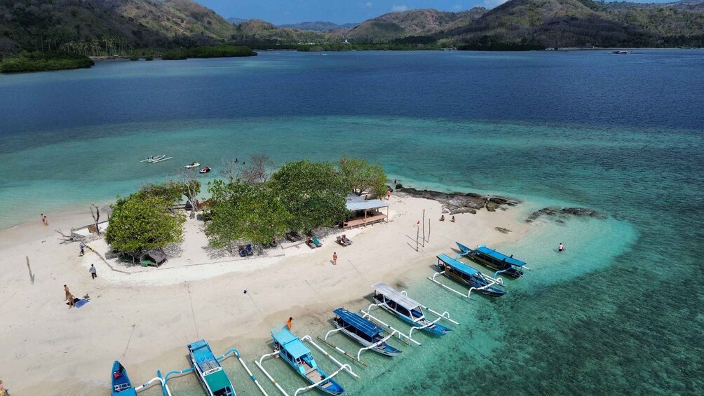A tropical island with clear turquoise waters, a sandy beach, and several traditional boats docked. 2