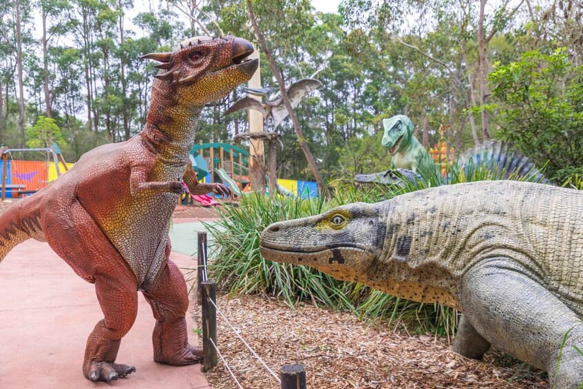 A dinosaur exhibit with a large red dinosaur and a green dinosaur in a naturalistic setting. 3