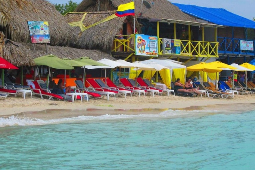 A beach with thatched-roof huts, colorful umbrellas, and red lounge chairs. 2