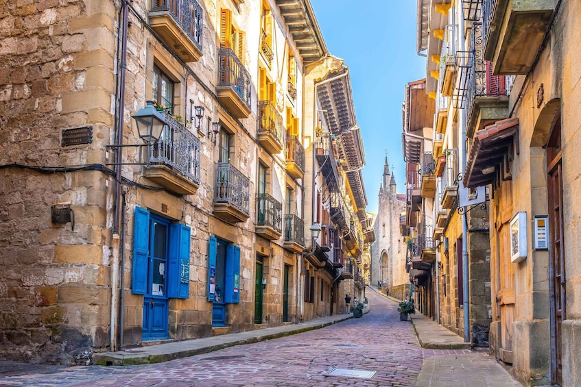 A cobblestone street lined with historic buildings, some with blue shutters and balconies. 1