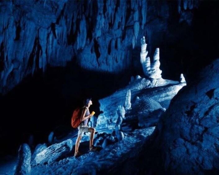 A person sitting on a rock formation in a cave with stalactites. 5