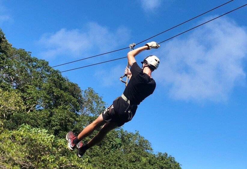 A person ziplining, wearing a helmet and harness, with trees and a clear sky in the background. 2