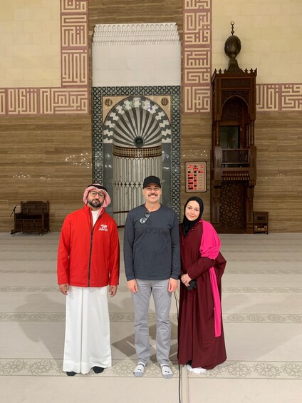Three people standing in front of a mosque with intricate geometric patterns and a large door. 3
