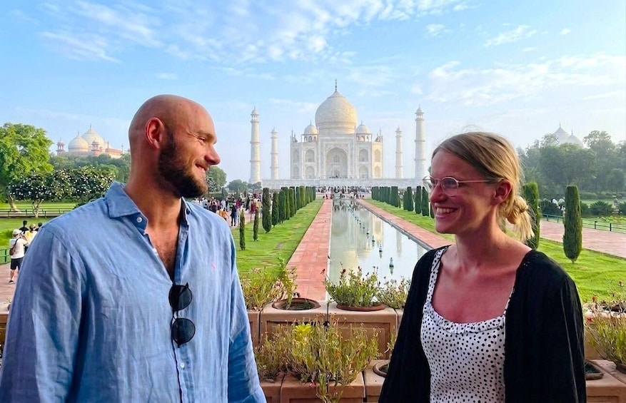 Two people standing in front of the Taj Mahal with a reflection pool and neatly trimmed hedges. 3