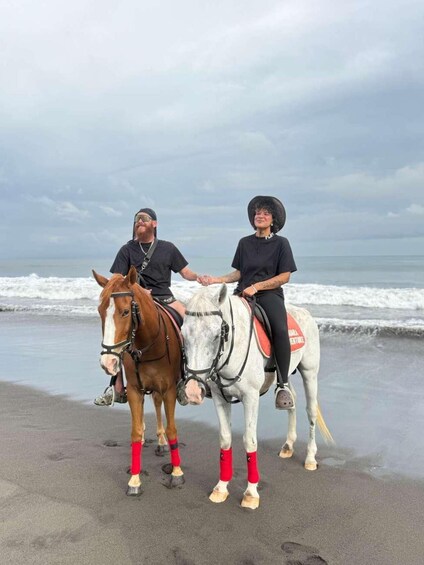 Two people riding horses on a beach with the ocean in the background. 4