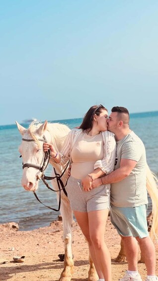A couple embracing a white horse on a beach with the sea in the background. 2